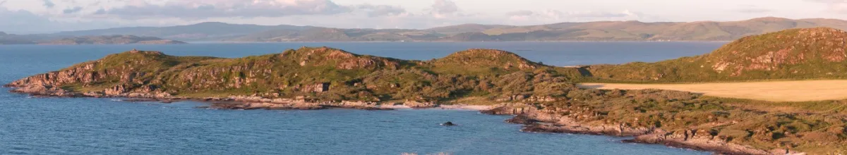 Küstenlinie von Gigha Raue Küstenlinie von Gigha bei Sonnenschein.