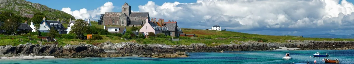 Blick von der Küste auf die Iona Abtei, mehrere Boote schwimmen im Vordergrund auf dem Meer.