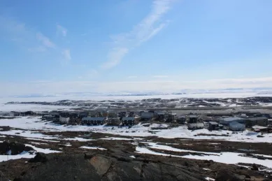 Iqaluit Eine kleine Häuseransammlung steht auf einer schneebedeckten Tundralandschaft.