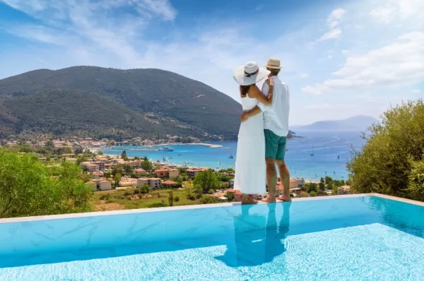 Die Aussicht über Lefkada Ein Pärchen, das am Rande eines Infinitypools steht und die Aussicht über die bergige, grüne Landschaft Lefkadas genießt.