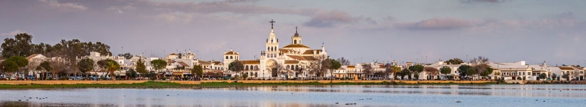 Blick auf das Stadtbild von Huelva mit der imposanten weißen Kirche in der Mitte, im Vordergrund Wasser.