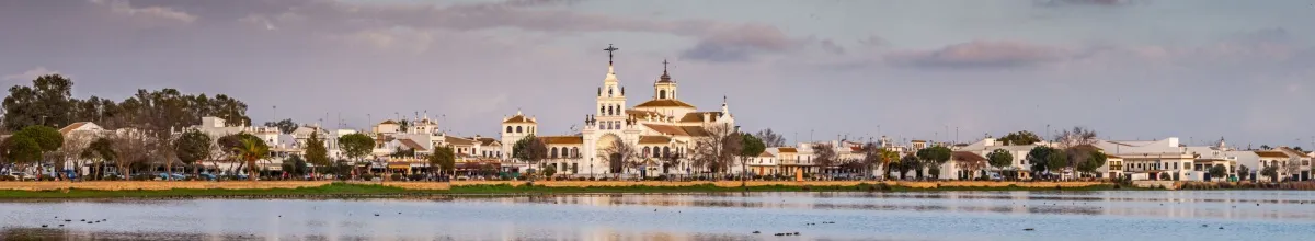 Blick auf das Stadtbild von Huelva mit der imposanten weißen Kirche in der Mitte, im Vordergrund Wasser.