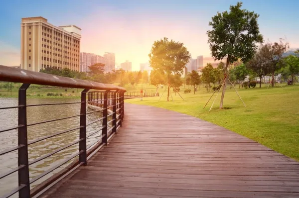 Shenzhen Stadtpark Ein Stadtpark in Shenzhen mit grüner Wiesenfläche und einem Holzsteg am Wasser, im Hintergrund sieht man die Wolkenkratzer.