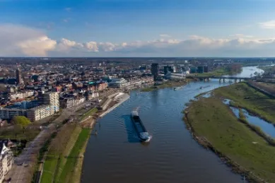 Blick auf die Stadt Venlo am Fluss mit vorbeifahrenden Schiffen unter blauem Himmel.