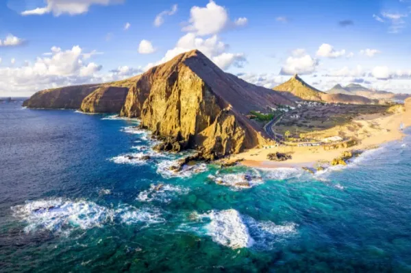 Ein Panoramafoto der Insel Porto Santo mit einem Felsmassiv im Vordergrund und dem aufschäumenden, tiefblauen Meer drumherum.