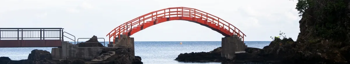 Eine rote Bogenbrücke auf Sado am Tag mit dem weiten Meer im Hintergrund.