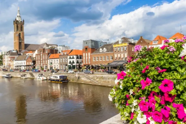 Roermond Gebäude und Kirche am Fluss mit kleinen Booten, im Vordergrund eine Brücke mit pinken Blumen.