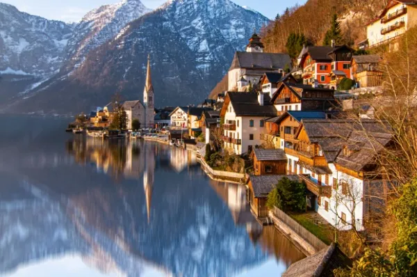 Fachwerkhäuser in Salzburg Alte Fachwerkhäuser am Ufer der Salzach in Salzburg und einer Kirche. Im Hintergrund sind schneebedeckte Berge zu sehen.