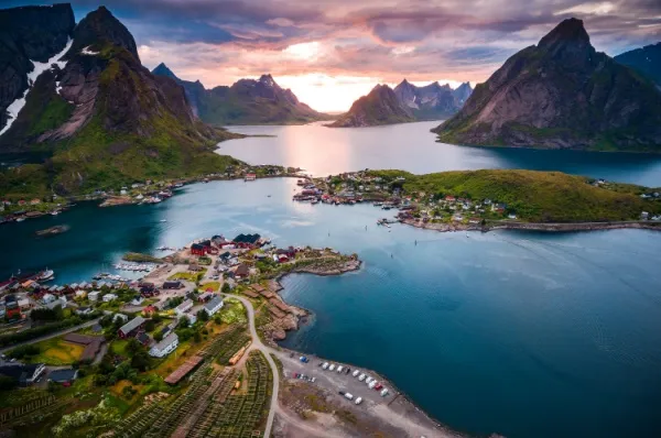 Reine & umliegende Inseln Die Sonne geht am Horizont zwischen Bergketten unter, im Vordergrund liegt Reine und die umliegenden Inseln.