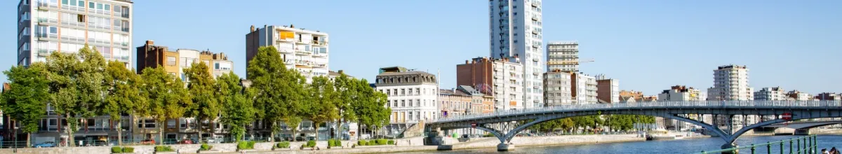 Flusspanorama der Stadt Lüttich mit Hochhäusern unter blauem Himmel.