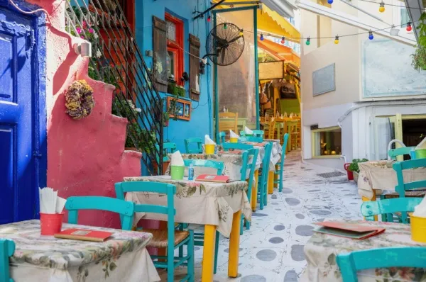 Bunte Stühle und Tische einer Taverne stehen in einer Gasse in Tinos.