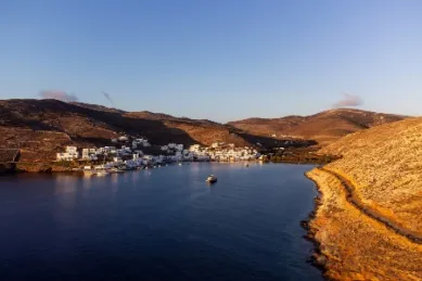 Die untergehende Sonne scheint auf die karge Küste von Tinos, Dorf mit weißen Häusern im Hintergrund.