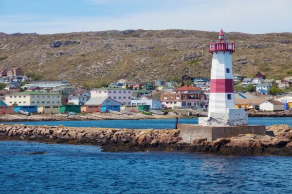 Leuchtturm von Saint-Pierre Der rot-weiße Leuchtturm von St. Pierre und Miquelon vor den bunten Häusern an der Küste.