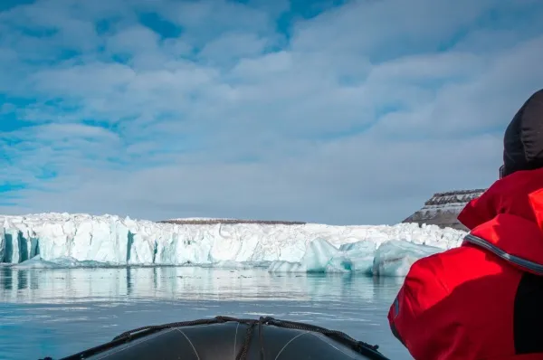 Ein Reisender in einer roten Winterjacke, der von einem Schiff aus auf die eisige Küste Crocker Bays blickt bei Tag.