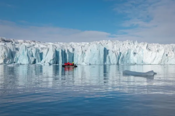 Eine Gruppe von Reisenden in roten Winterjacken an Bord eines Schlauchbootes, das tagsüber entlang der Küste von Crocker Bay segelt.
