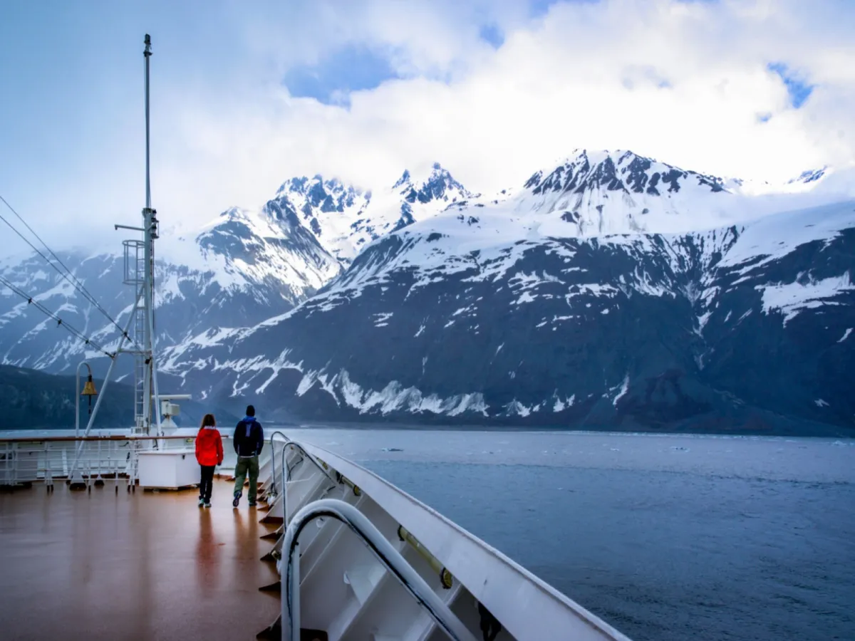 Zwei Reisende an Deck eines Schiffes in der Region von Crocker Bay mit riesigen, schneebedeckten Bergen im Hintergrund und dem stillen Meer, das sie voneinander trennt.