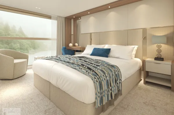 Kabine mit absenkbarer Panorama-Fensterfront auf dem Mozart & Strauss Deck (Rendering) Rendering Doppelbett in einer Außenkabine mit absenkbarem Panoramafenster mit Flussblick auf der AMADEUS Amara. Auf dem weiß bezogenen Bett liegen 2 weiße & 1 blaues Kissen & 1 bunte Decke, dahinter stehen 1 Sessel & 1 Schreibtisch mit Stuhl.
