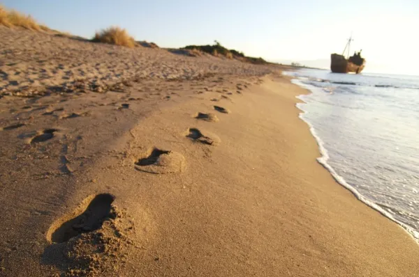 Nahaufnahme eines Sandstrands, im Hintergrund ein altes Schiffwrack.