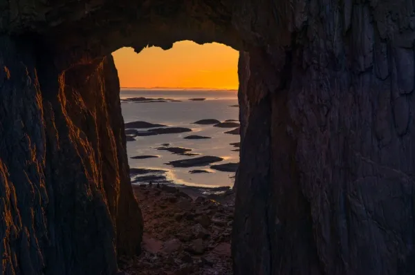 Der Sonnenuntergang und kleine Inseln im Ozean sind durch das Loch im Berg Torghatten sichtbar.