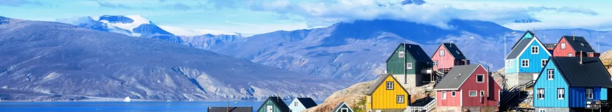 Die bunten Häuser Uummannaqs ganz  oben auf einer Anhöhe mit einer Berglandschaft im Hintergrund.