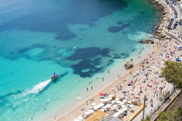 Der Strand von Villefranche-Sur-Mer aus der Vogelperspektive. Ein Boot fährt an der Küste entlang und wirbelt das Wasser auf.