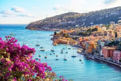 Villefranche-Sur-Mer auf der Höhe fotografiert bei fantastischem Wetter mit pinken Blumen im Vordergrund.