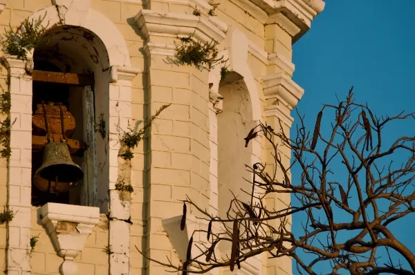 Glockenturm Vigan City Ein Ausschnitt eines Glockenturms in der Nahaufnahme. Die Glocke lugt durch ein Fenster, im Vordergrund sind Äste ohne Blätter.