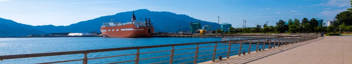 Ein riesiges, rotes Schiff am Hafen von Tsuruga mit den Bergen des Festlands im Hintergrund am Tag.