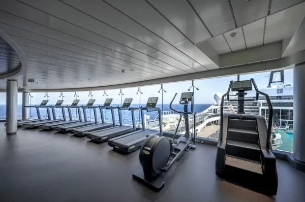 Fitnessstudio auf MSC World America Fitnessstudio mit Meer- & Poolblick. Vor einer Glasfront stehen sieben Laufbänder, ein Crosstrainer und ein Stairmaster.