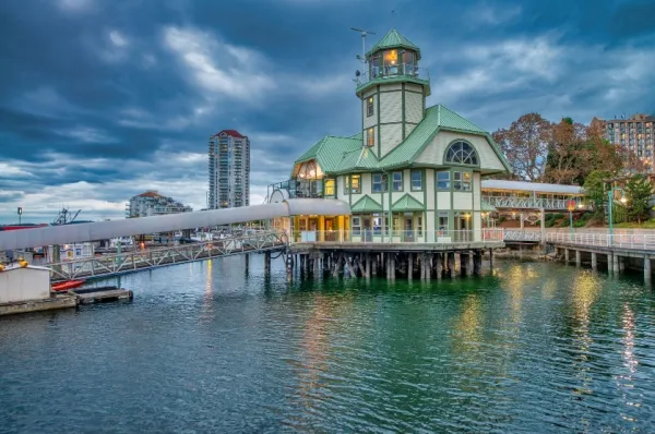 Nanaimo Besonderes Haus auf einem Holzsteg auf dem Wasser, im Hintergrund ein Hochhaus.