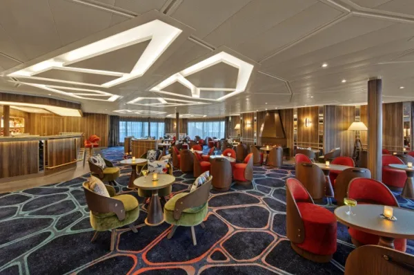 Lounge Koningsdam Eine Lounge mit bequemen Sesseln und runden Tischen.