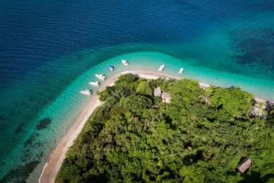 Ein Strand mit kleinen Booten aus der Vogelperspektive mit grünem Inland.