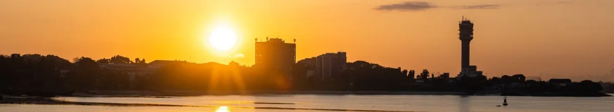 Die Skyline von Daressalam mit einem großen Turm im orangenen Schein des Sonnenuntergangs.
