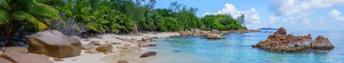 Der Strand von Curieuse als Panorama, mit Granitfelsen, die aus dem Sand empor steigen und der grünen Vegetation.