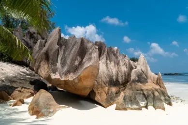 Ein riesiger Granitfelsen ragt aus dem Strand auf Curieuse. Im Hintergrund ist strahlend blauer Himmel zu sehen.