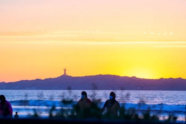 Coquimbo Sonnenuntergang Ein orangener Sonnenuntergang hinter den Bergen von Coquimbo. Die Silhouette des großen Kreuzes ist zu sehen. Im Vordergrund sind Menschen.