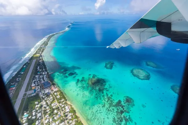 Aufgenommen ist das Funafuti Atoll aus dem Flugzeug aus. Zu sehen ist ein Flügel, das Meer mit den Riffen und die Insel.