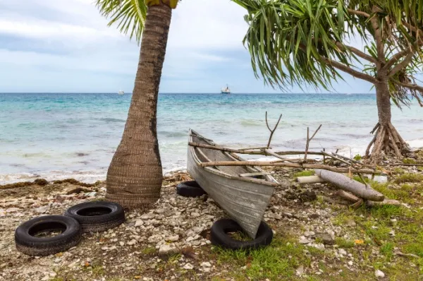 Ein Paddelboot unter einer Palme am Strand von Funafuti mit dem Meer im Hintergrund.