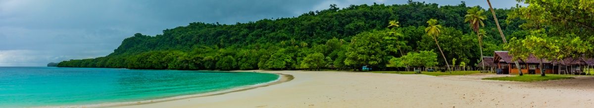 Der Strand von Luganville mit champagnerfarbenen Sand und Regenwand im Hintergrund, der an türkises Wasser mündet.