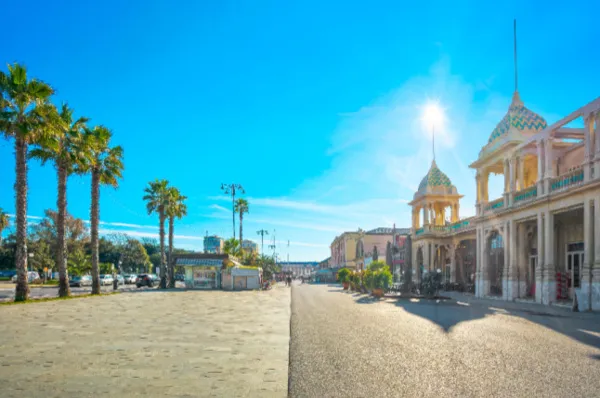 Strandpromenade im Sonnenschein Die Strandpromenade von Viareggio im Sonnenschein mit Palmen und Sand links und rechts einem alten Gebäude.