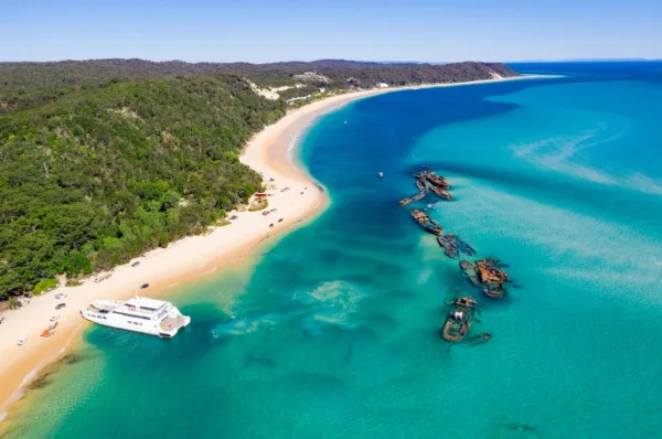 Die Küste der Moretoninsel mit Wäldern, Sandstrand und Wracks im Wasser. Ein Schiff ankert.