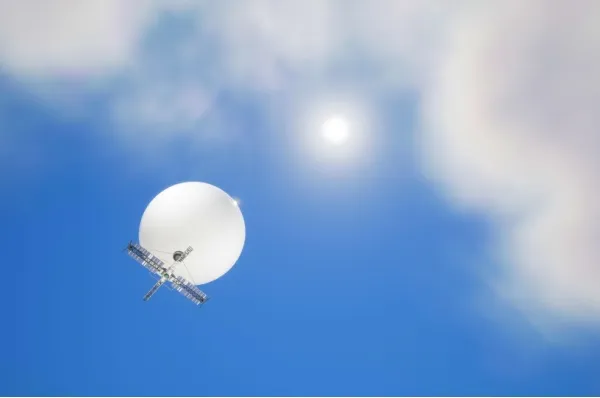 Ein weißer Wetterballon mit einer kleinen Solaranlage fliegt gen Himmel mit Wolken. Die Sonne scheint.