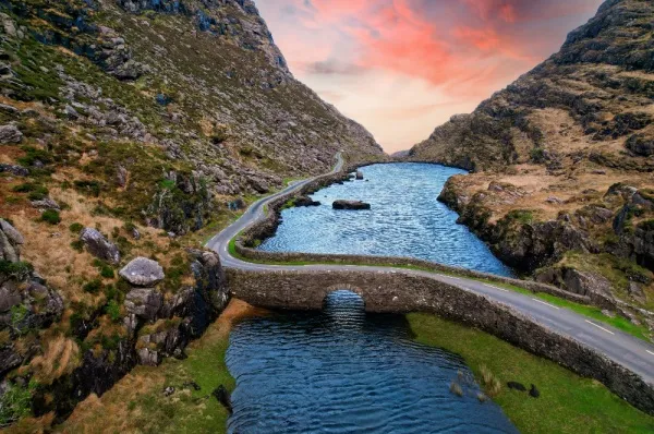 Luftsicht auf Sonnenuntergang an der Stein-Wunschbrücke über Fluss im grünen Tal bei der Gap of Dunloe.