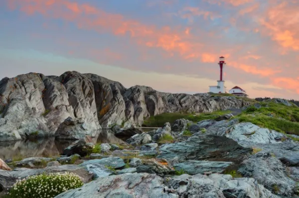 Der Leuchtturm Cape Forchu von Yarmouth ragt im Sonnenuntergang auf der felsigen Landschaft empor.
