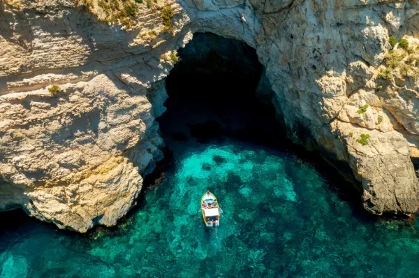 Eine kleine Yacht schwimmt vor dem Eingang zu einer Bucht in einem Felsen.