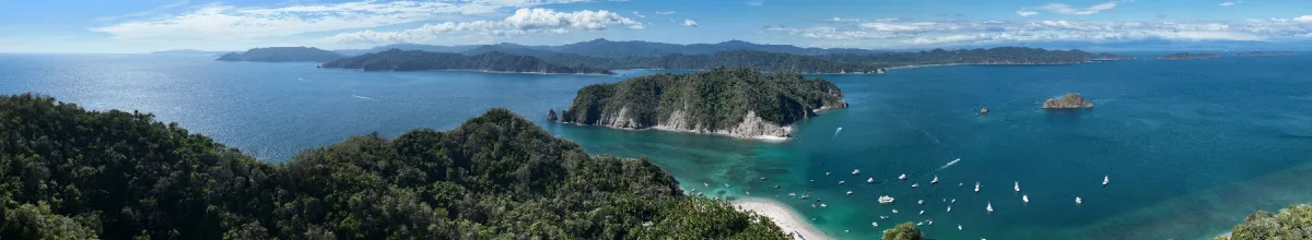 Luftaufnahme der Küste der Isla Tortuga mit vielen kleinen Schiffen auf dem Wasser und den üppig bewachsenen Nachbarinseln im Hintergrund.