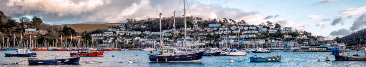 Segelboote vor Anker im Hafen von Dartmouth am Tag, mit der Stadt im Hintergrund.