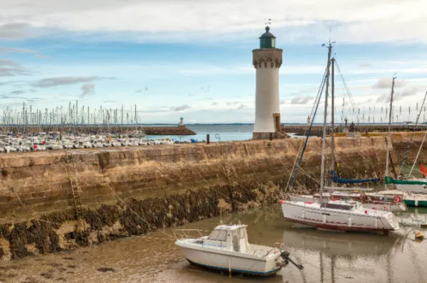 Der Hafen von Quiberon am Tag mit einigen Booten vor Anker, einer steinernen Kaimauer und einem Leuchtturm um Hintergrund.