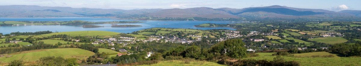 Grüne, hügelige Landschaft mit der Bantry Bay im Hintergrund.