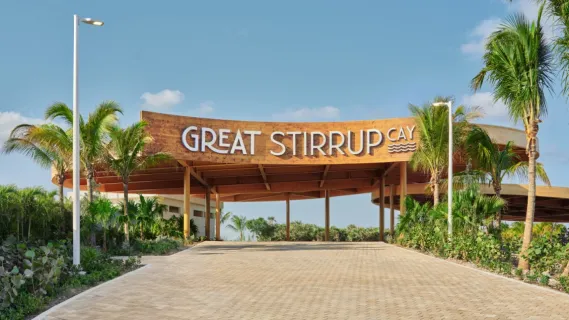 Willkommen auf Great Stirrup Cay Der neu gestaltete Eingang von Great Stirrup Cay mit einem großen Willkommensschild. Der Gehweg ist von Palmen umsäumt.